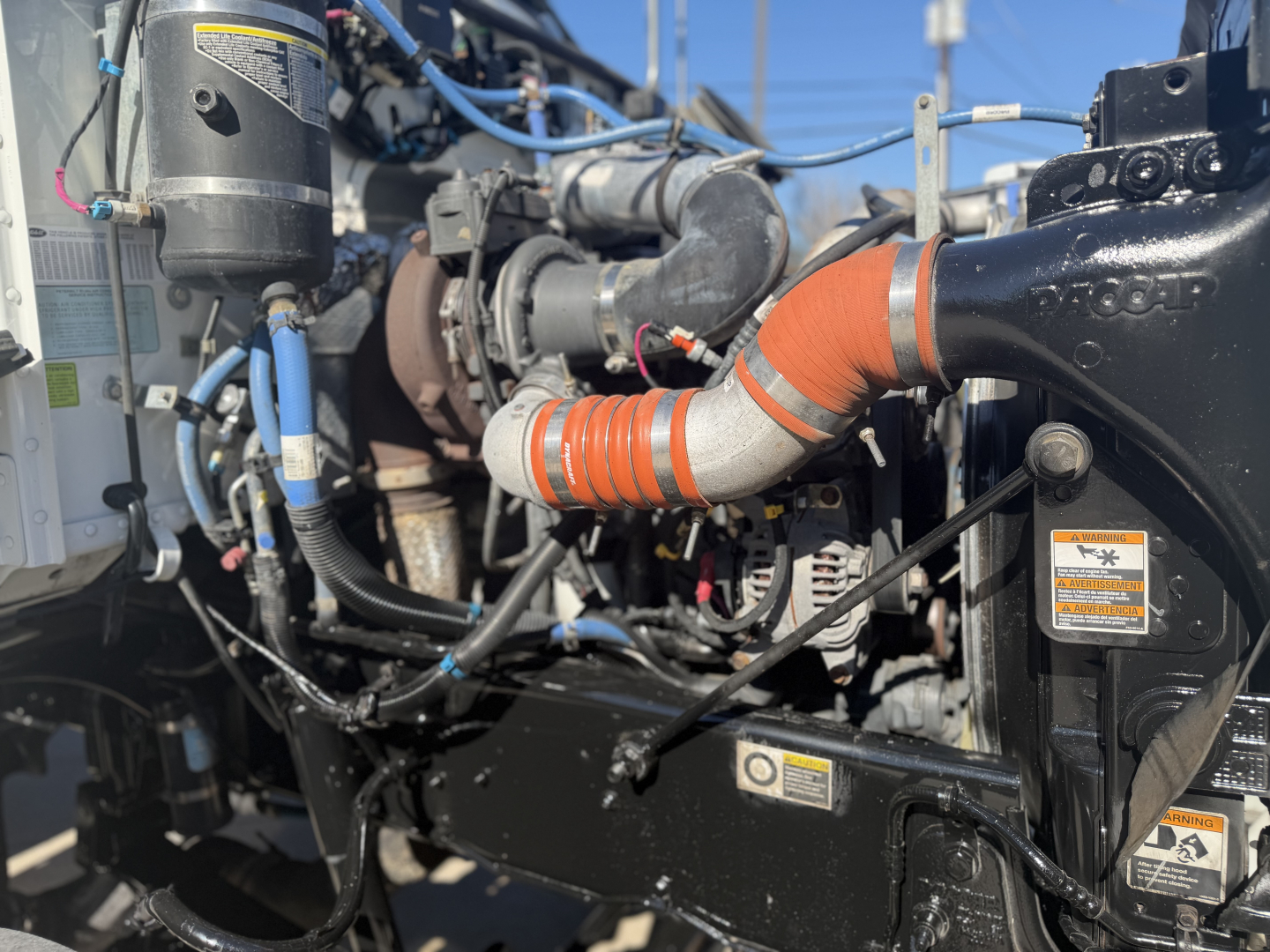Peterbilt engine bay showing orange coolant hose, black radiator/turbo housing, wiring harness, and various labels/stickers.