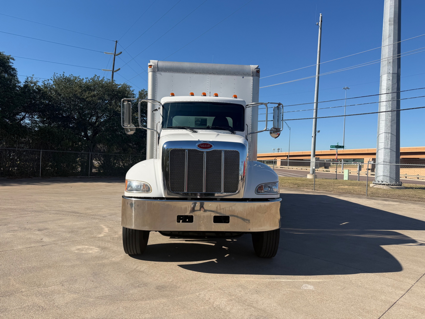 Peterbilt 337 box truck front view with large grille and chrome bumper, white cab, daytime outdoors.