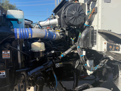 Peterbilt 337 engine bay with blue intake hose, various components, wiring harnesses, and a white box truck side in view.