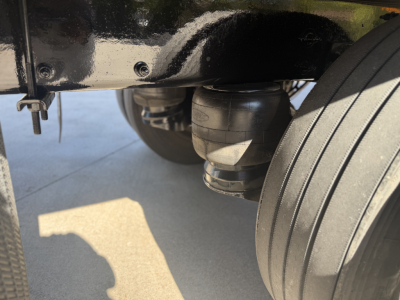 Peterbilt 337 rear undercarriage showing air suspension bag and dual rear tires; visible frame with black paint and a plug/connector near the axle. No legible labels or serials readable.