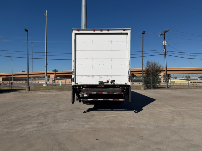 Rear view of a white Peterbilt box truck trailer with a raised rear doors, taillights, and bumper reflecting in a paved lot.