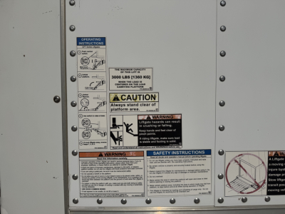 Truck side panel with multiple safety and operation stickers including load capacity and warnings on a Peterbilt 337 box truck.