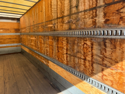 Truck trailer interior showing wooden panels and silver E-Track rails along the side walls.