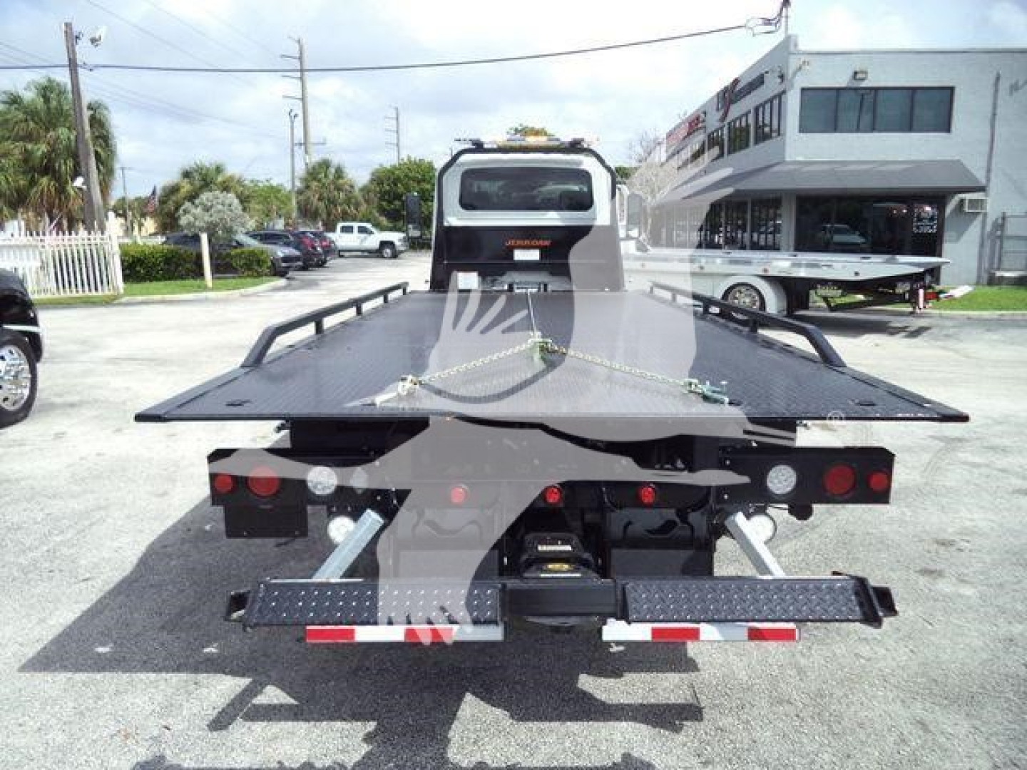 Flatbed tow truck bed on a 2027 International MV rollback truck showing rear view with taillights, hydraulic components, and loading deck.