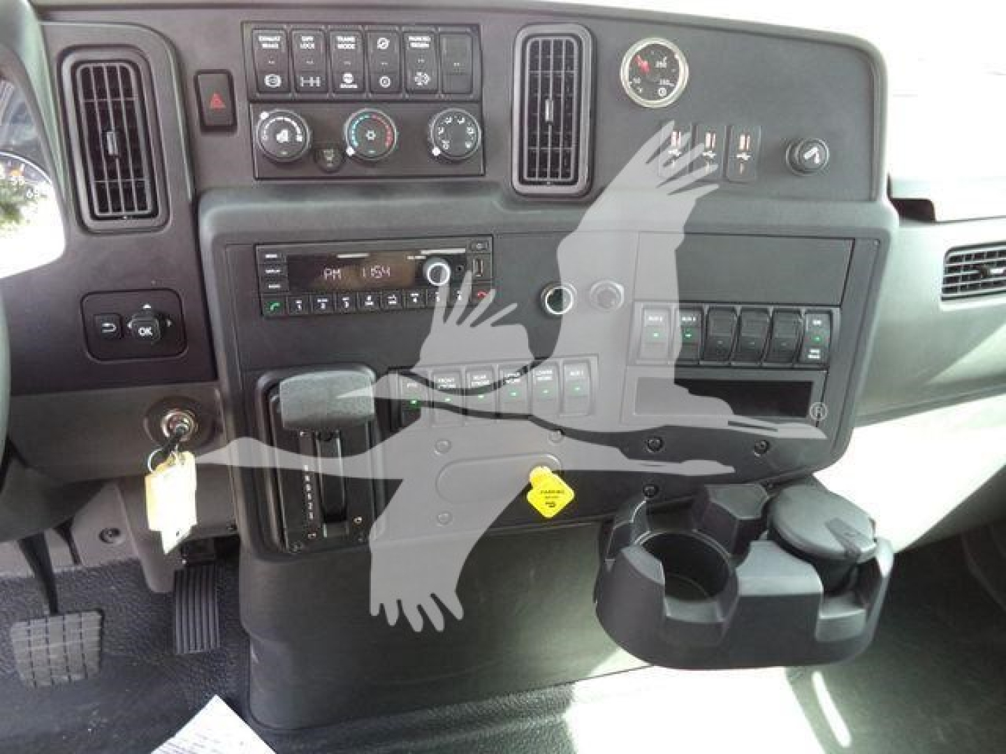 Truck dashboard and console showing steering column, instrument cluster, HVAC controls, and cup holder from International MV cab interior.