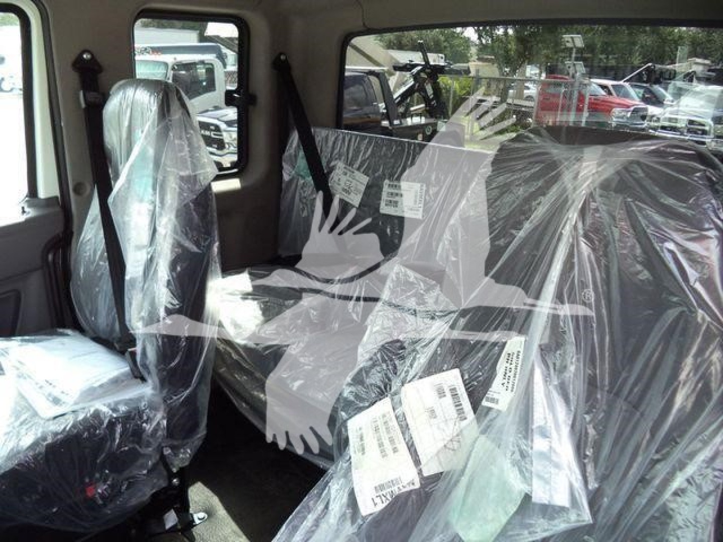Truck cab interior with plastic-covered seats and seating labels/tags visible, window views of other trucks in lot.