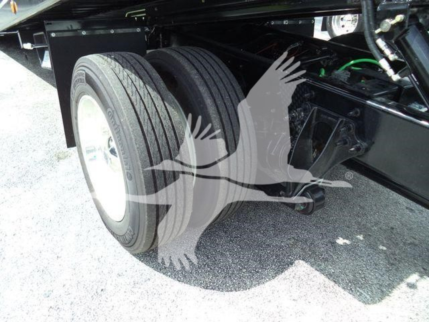 Truck rear dual tires and suspension visible under a rollback truck, with black chassis and green wiring; part of the undercarriage and wheel assembly visible.