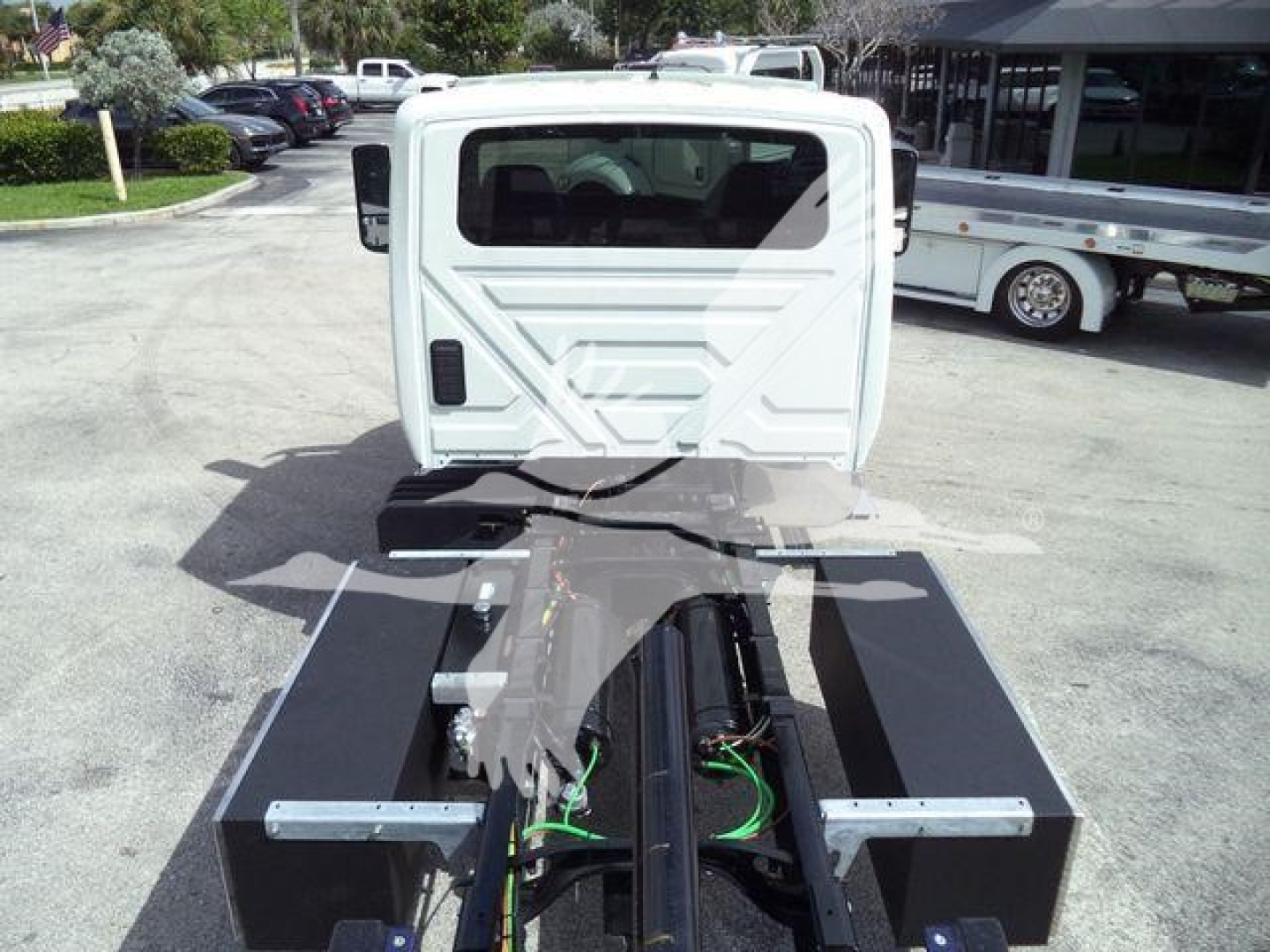 Truck chassis with cab and frame showing rollback configuration, rear view of cab, green and black cables, metal side rails.