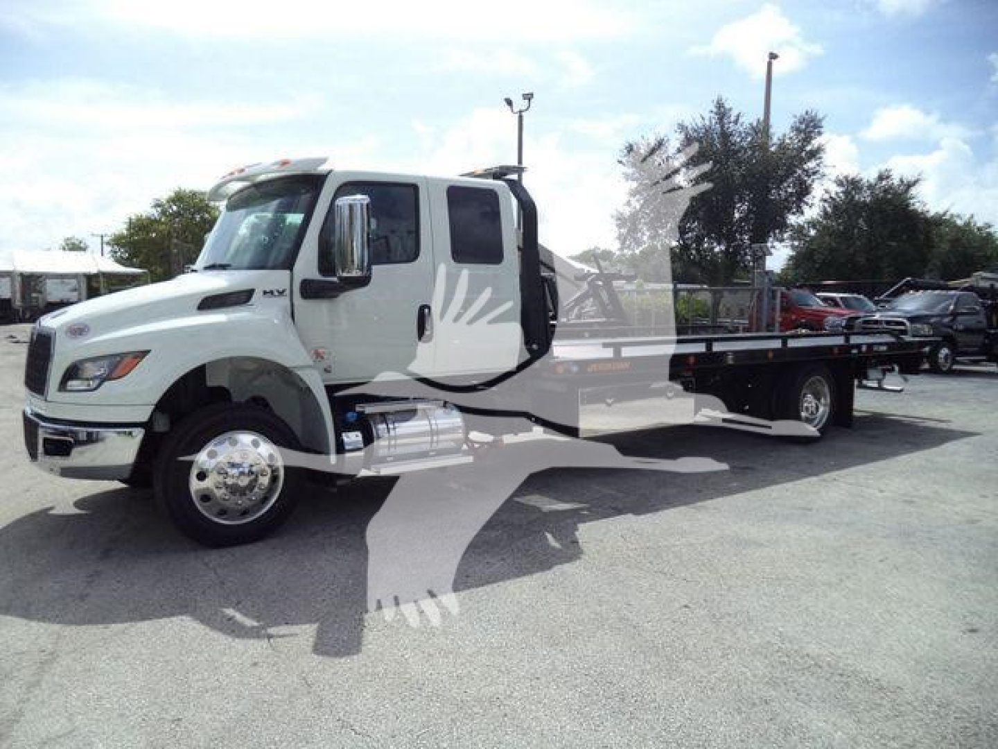 Truck in a dealership lot showing a white International MV rollback w/ dual rear wheels and flatbed