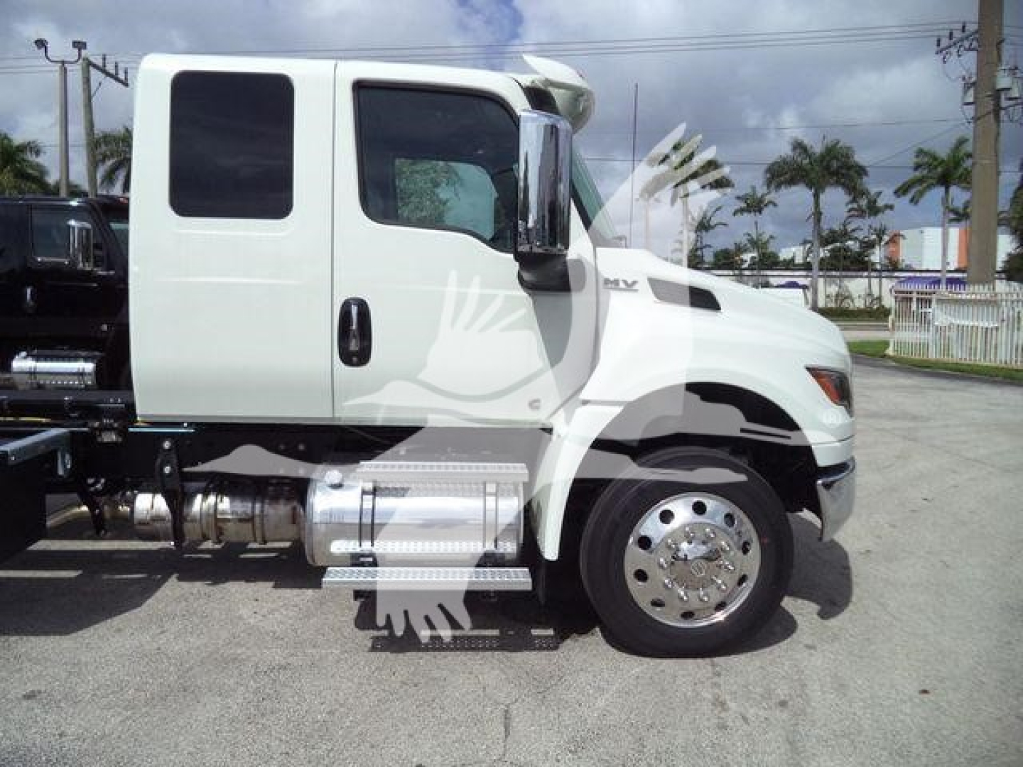 Truck side view showing white International MV cab with chrome fuel tanks and steps, black wheel arch, and dual rear wheels.