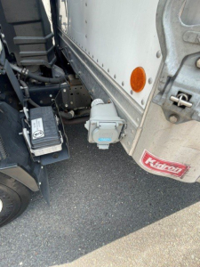 Isuzu NQR reefer truck side with auxiliary electrical box and power inlet visible near cab corner.