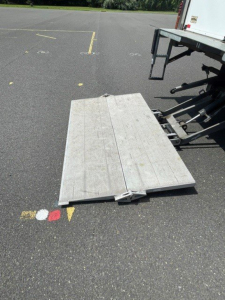 Isuzu NQR truck with a fold-out metal ramp on a loading dock, visible attached to a box van truck.