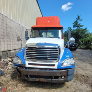 Front view of a Freightliner Columbia 120 conventional truck with blue fenders and orange cab roof. Visible grille and bumper, daytime outdoor lot.