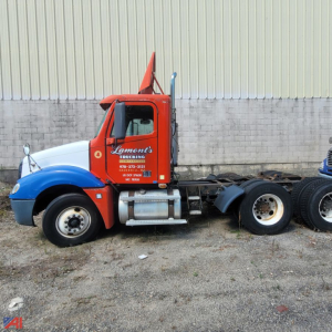 Truck cab side view showing red Lament's Express truck with blue fenders and Freightliner Columbia 120 chassis, labeling on door, fuel tank, exhaust stack, and dual rear wheels.