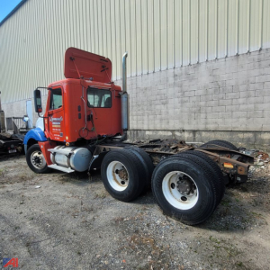 Freightliner Columbia 120 tractor cab in red with double rear axles and exposed fifth-wheel chassis; blue fender near front, truck in yard.
