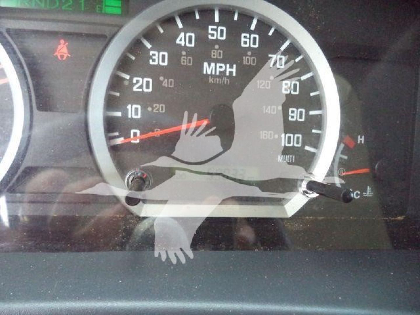 Isuzu dashboard showing speedometer with MPH and km/h markings, warning indicators, and a partial reflection.