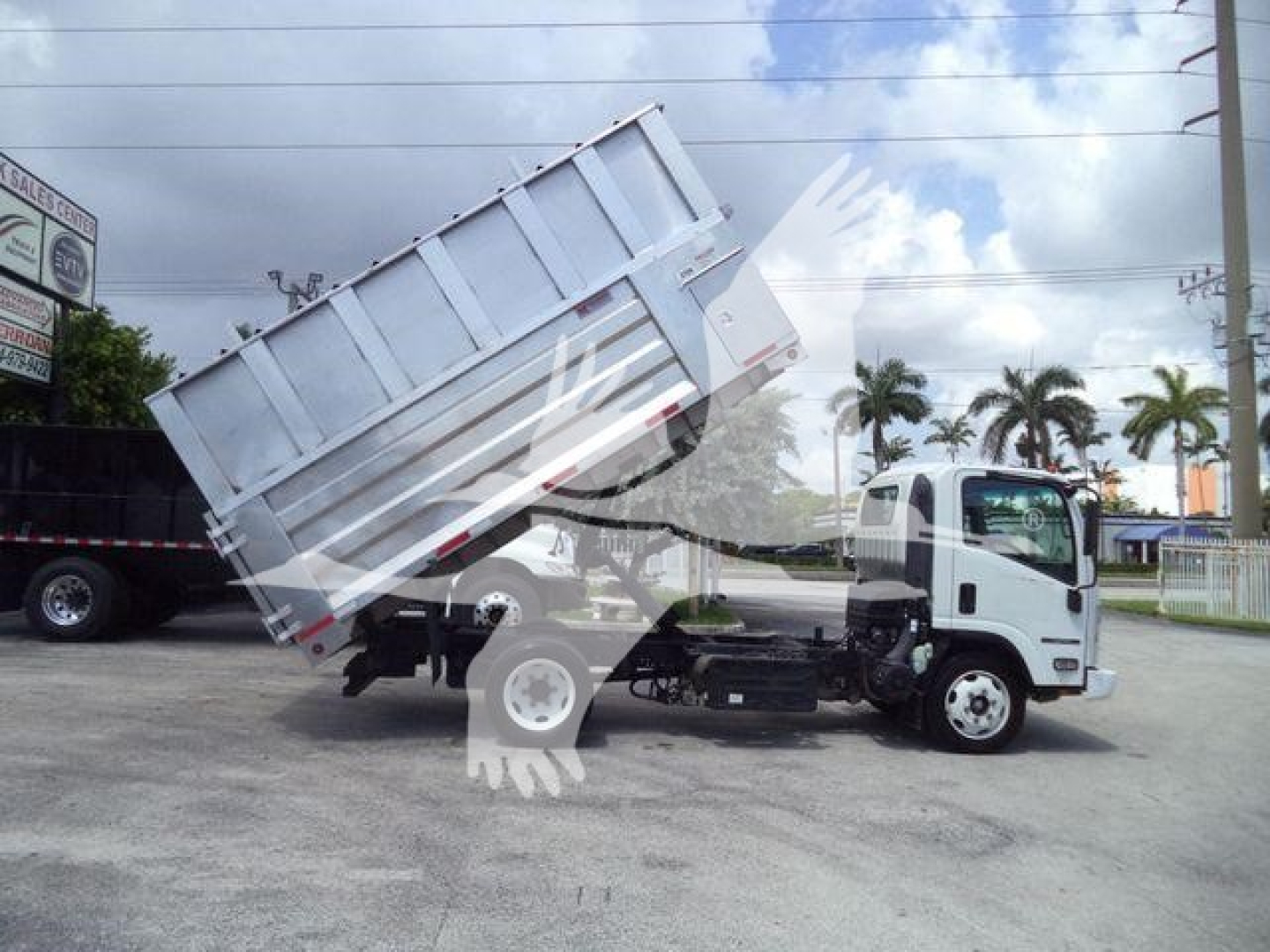 Isuzu NPR XD cab chassis truck with a raised dump bed in a dealership lot.