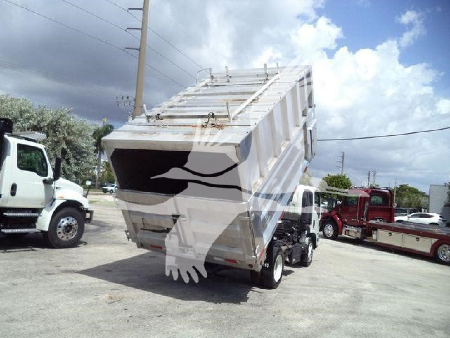 Isuzu NPR XD truck with a raised dump bed in a parking lot, rear view showing hydraulic dump mechanism and metal container.