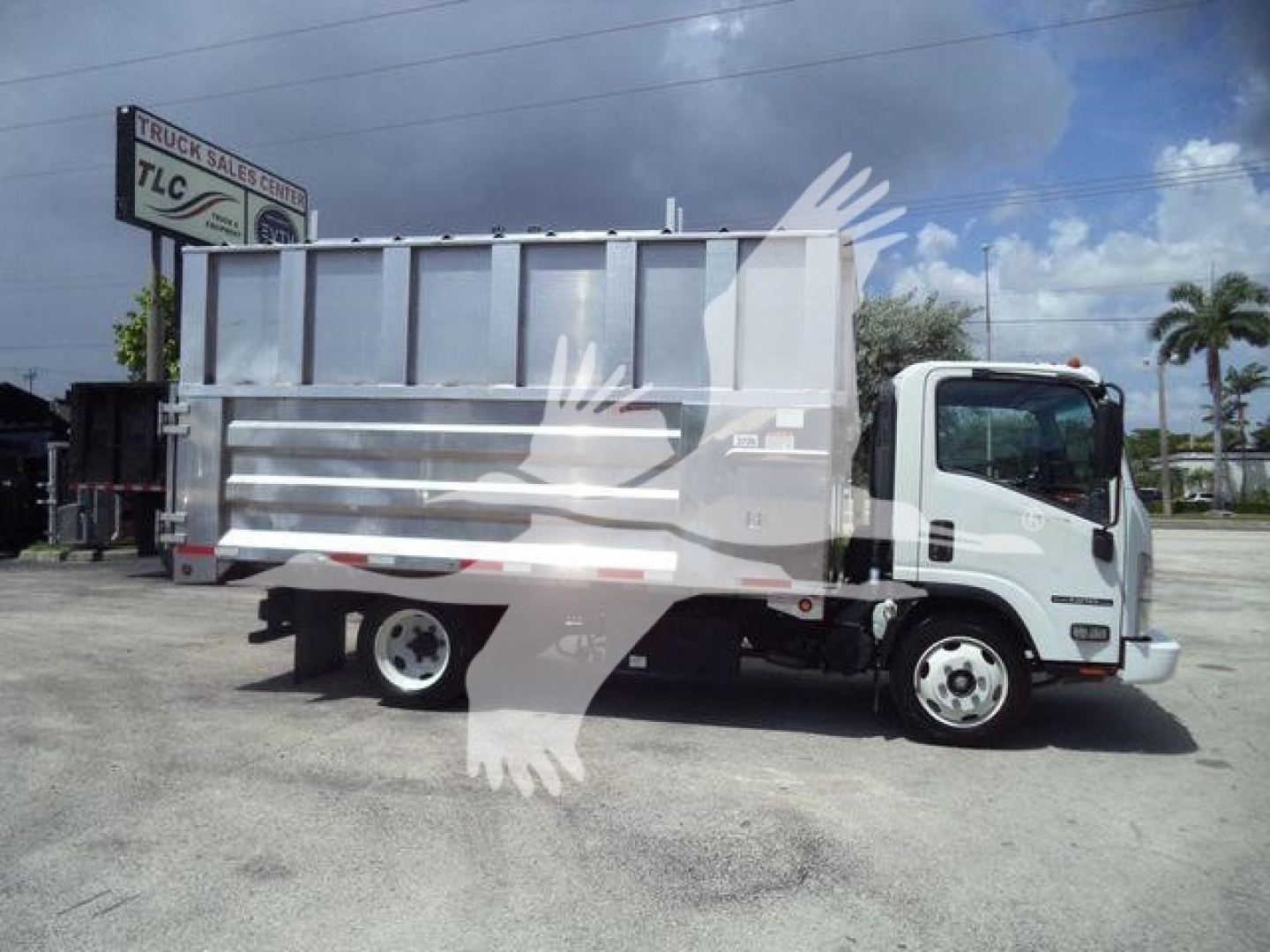 Isuzu NPR XD dump truck side view showing cargo bed and cab with TLC Truck Sales Center sign in background.