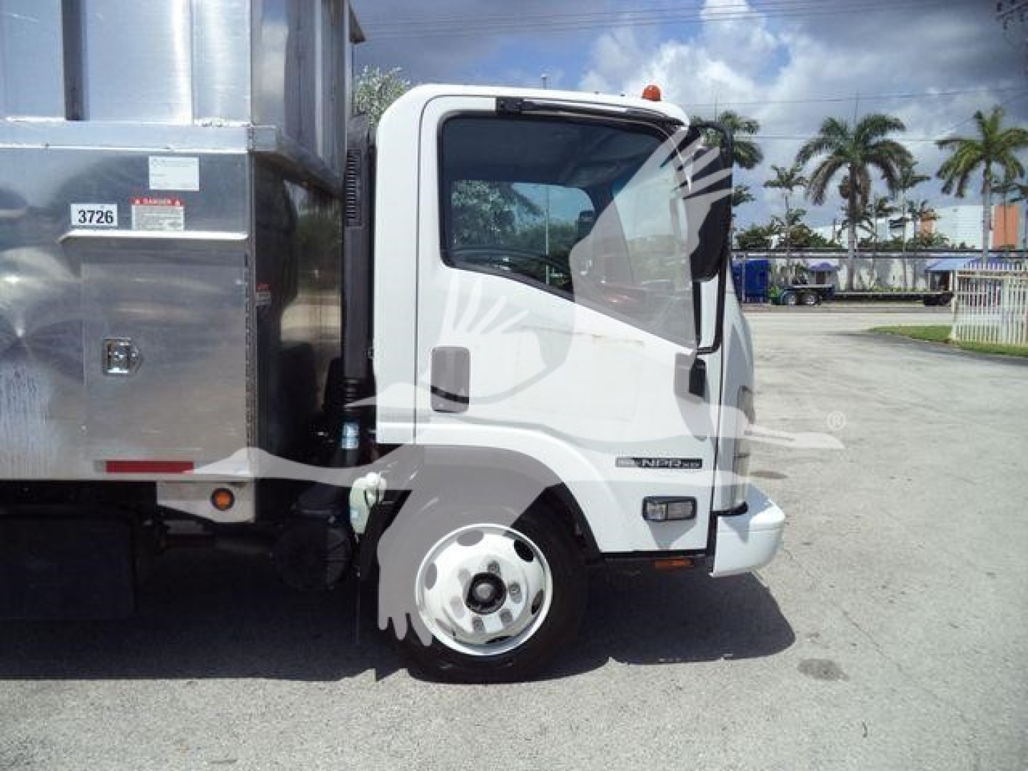 Isuzu NPR XD medium duty truck cab and front wheel with white cab and black bumper, side view, in chipper service setting.