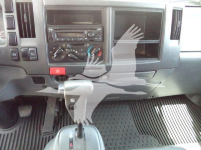 Isuzu NPR-XD dash area showing gear shifter, center console, climate controls, radio, and empty passenger door panel; grey interior with rubber floor mats.