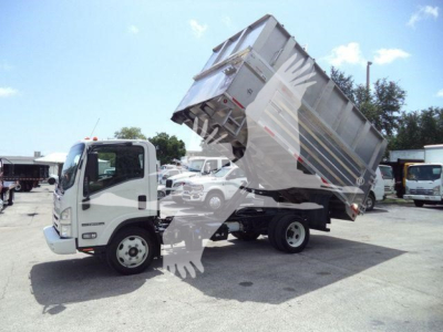 Isuzu NPR XD dump truck in service position with bed raised, showing cab and chassis, and surrounding lot of trucks.
