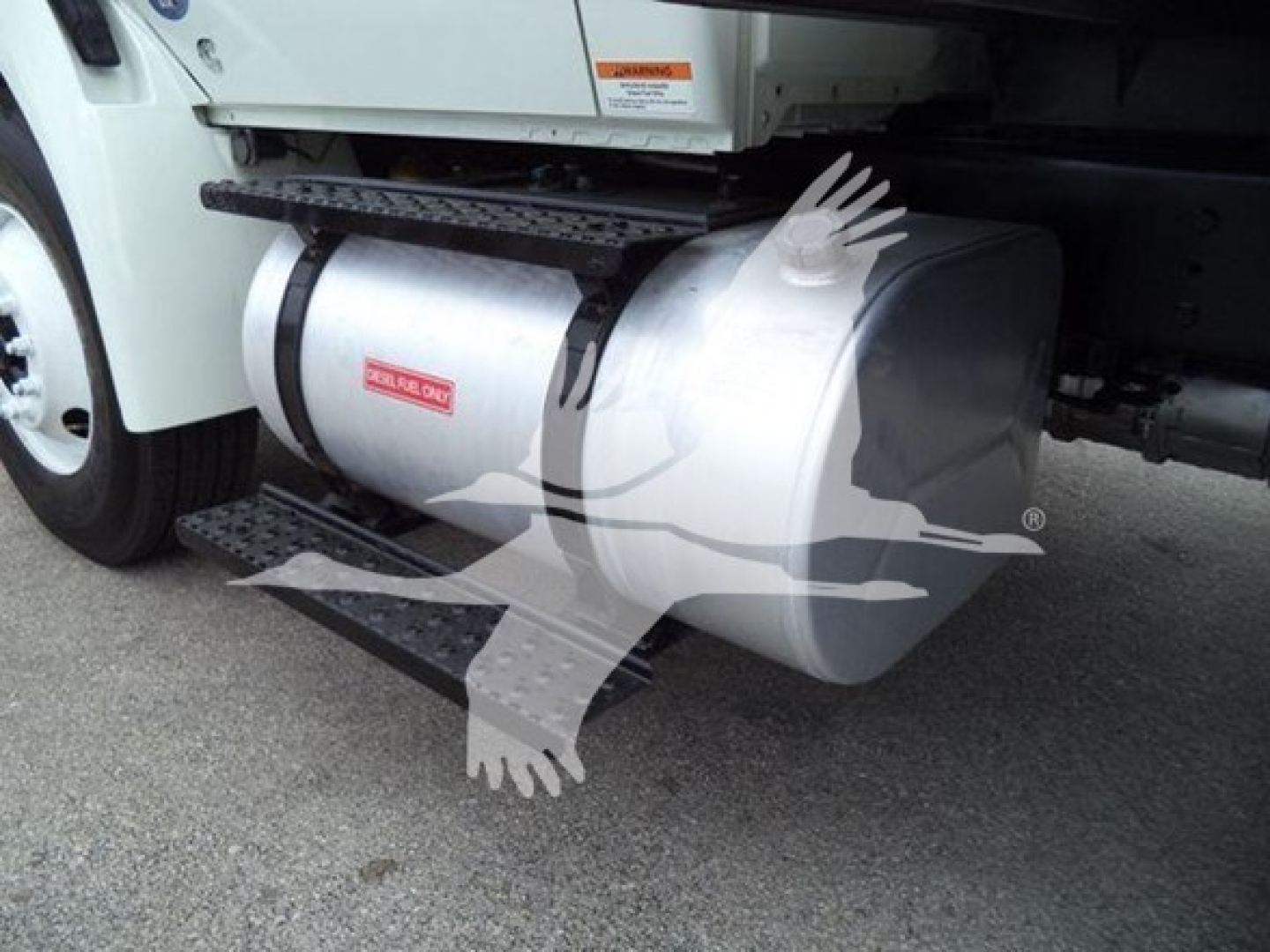 Fuel tank under International Durastar 4300 truck showing large aluminum cylindrical tank and side step, with warning labels visible.
