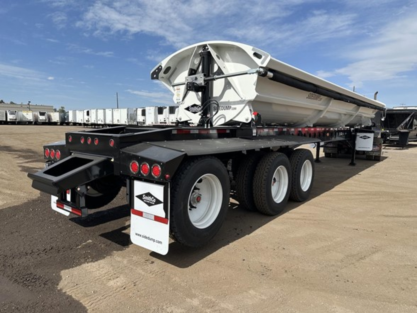 Smithco 2026 tri-axle air ride side dump trailer viewed from rear-left angle showing multiple axles, white wheels, and hydraulic components.