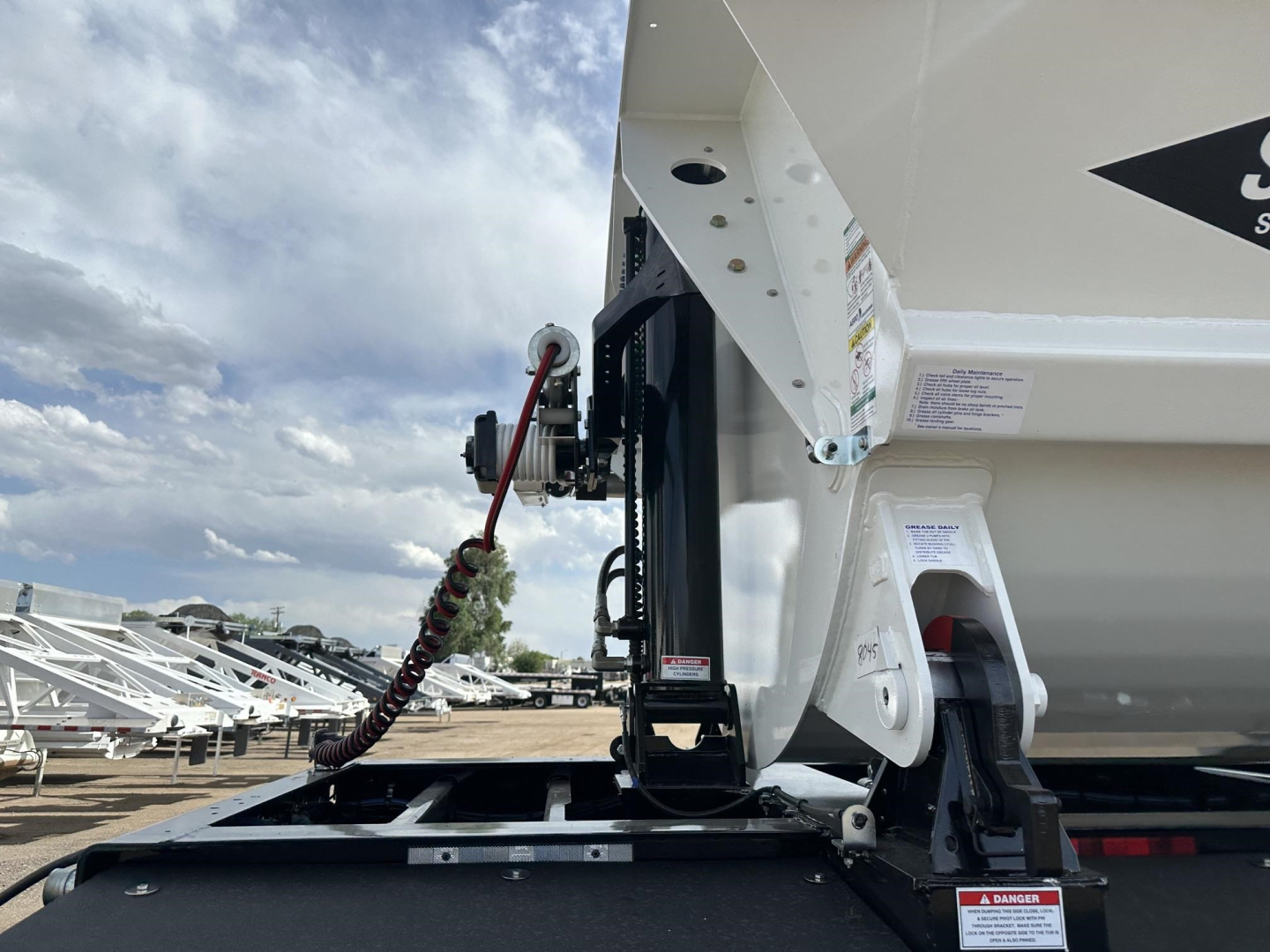 Side view of 2026 Smithco Side Dump trailer showing hydraulic lift mechanism and chute assembly with warning labels