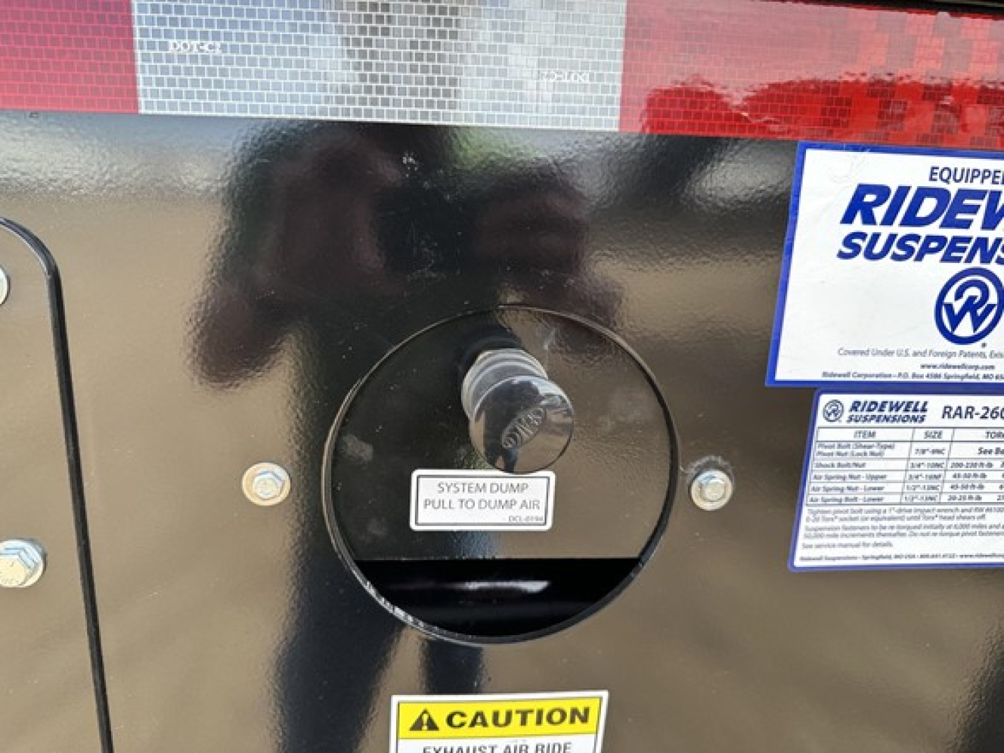 Tri-axle air ride side dump trailer access hatch with label ‘SYSTEM DUMP PULL TO DUMP AIR’ and surrounding decals.