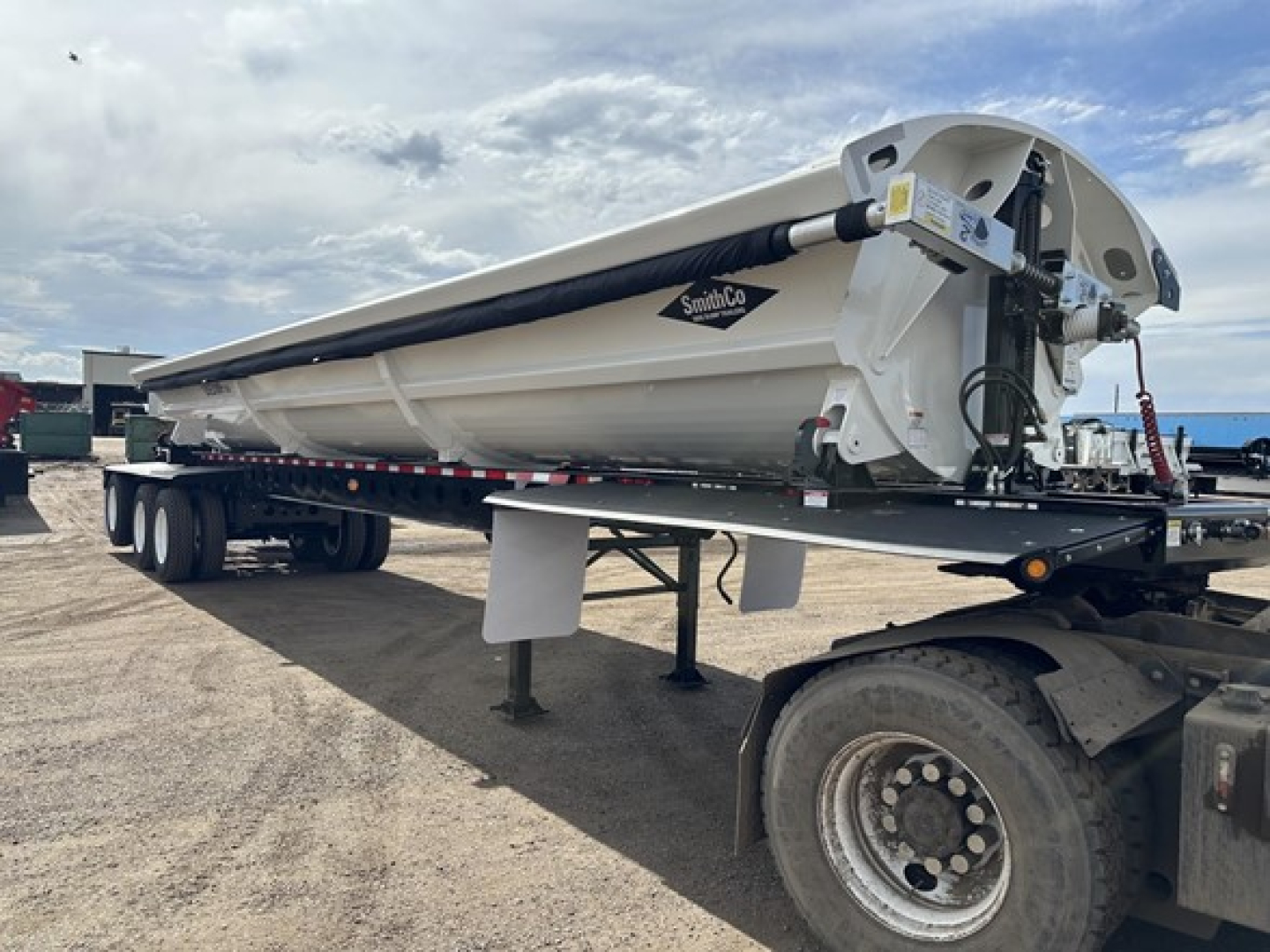 Smithco tri-axle air ride side dump trailer on semi truck chassis showing white cargo box and hydraulic lift components.