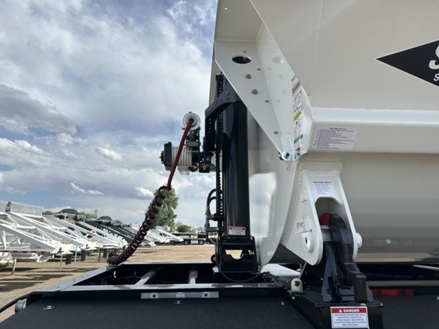 Front left side of a 2026 Smithco tri-axle air ride side dump trailer showing hydraulic system and hitch.