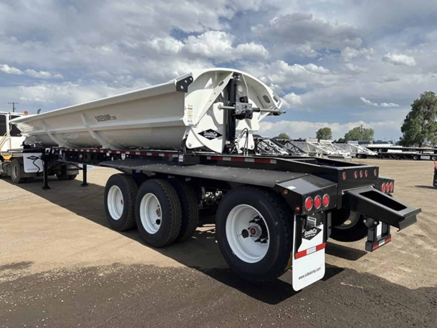 Tri axle air ride side dump trailer showing white bed and black undercarriage with dual rear axles and rear mud flaps