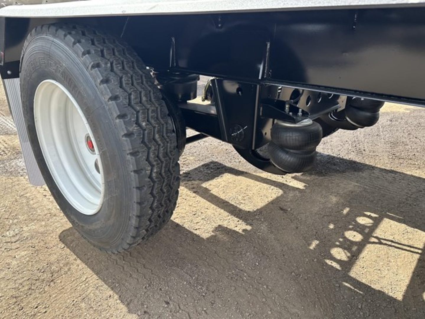 Trailer undercarriage with a large tire and air ride suspension showing coil springs and hoses; black frame and white wheel rim.