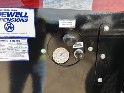 [Component] Gauge panel and labels on trailer front showing Pow traction? but clearly a pressure gauge with warning label and Dewell Pensions sticker; visible text includes 'Dewell Pensions' and 'G...AR-260' on blue label.