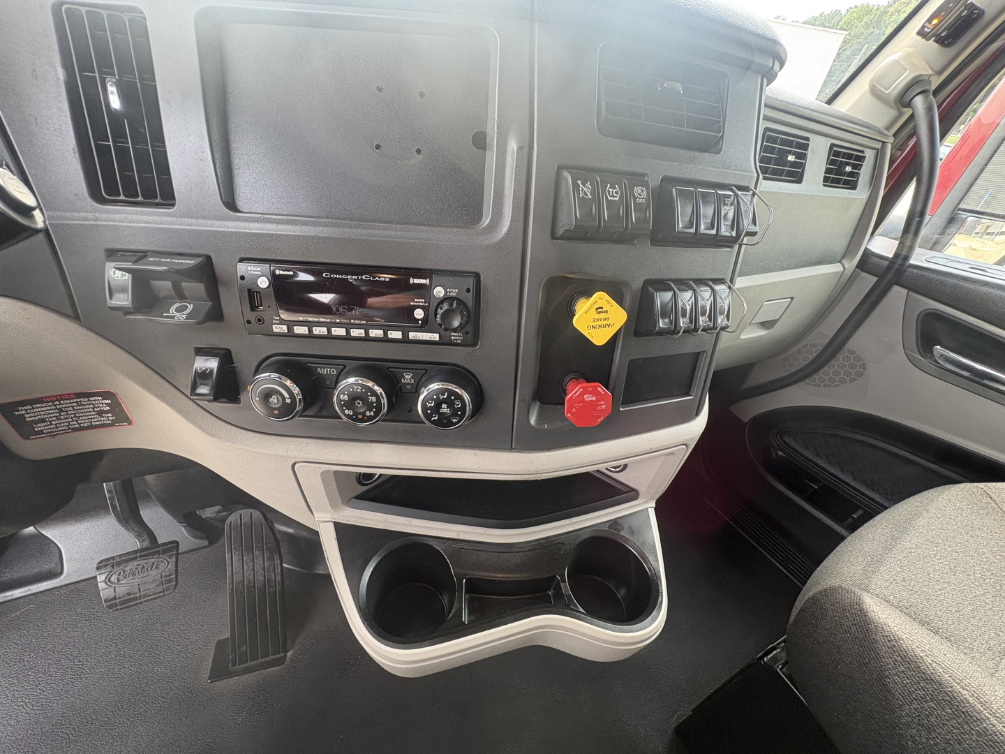 Peterbilt 579 cab interior dashboard view showing control switches, cup holders, and steering area. Visible text includes various knobs and a yellow service indicator tag.