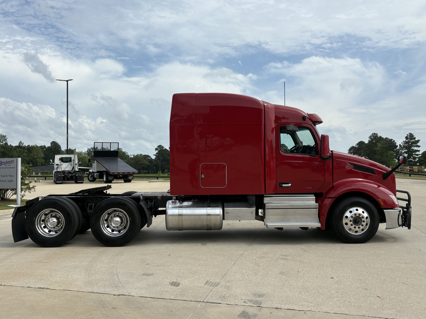 Peterbilt 579 tractor in red parked in lot, side view showing cab with sleeper and chrome fuel tanks; no text visible on body beyond general design.
