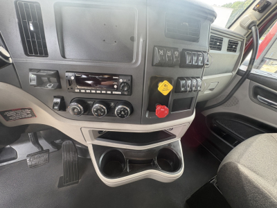 Peterbilt 579 cab interior dashboard view showing control switches, cup holders, and steering area. Visible text includes various knobs and a yellow service indicator tag.