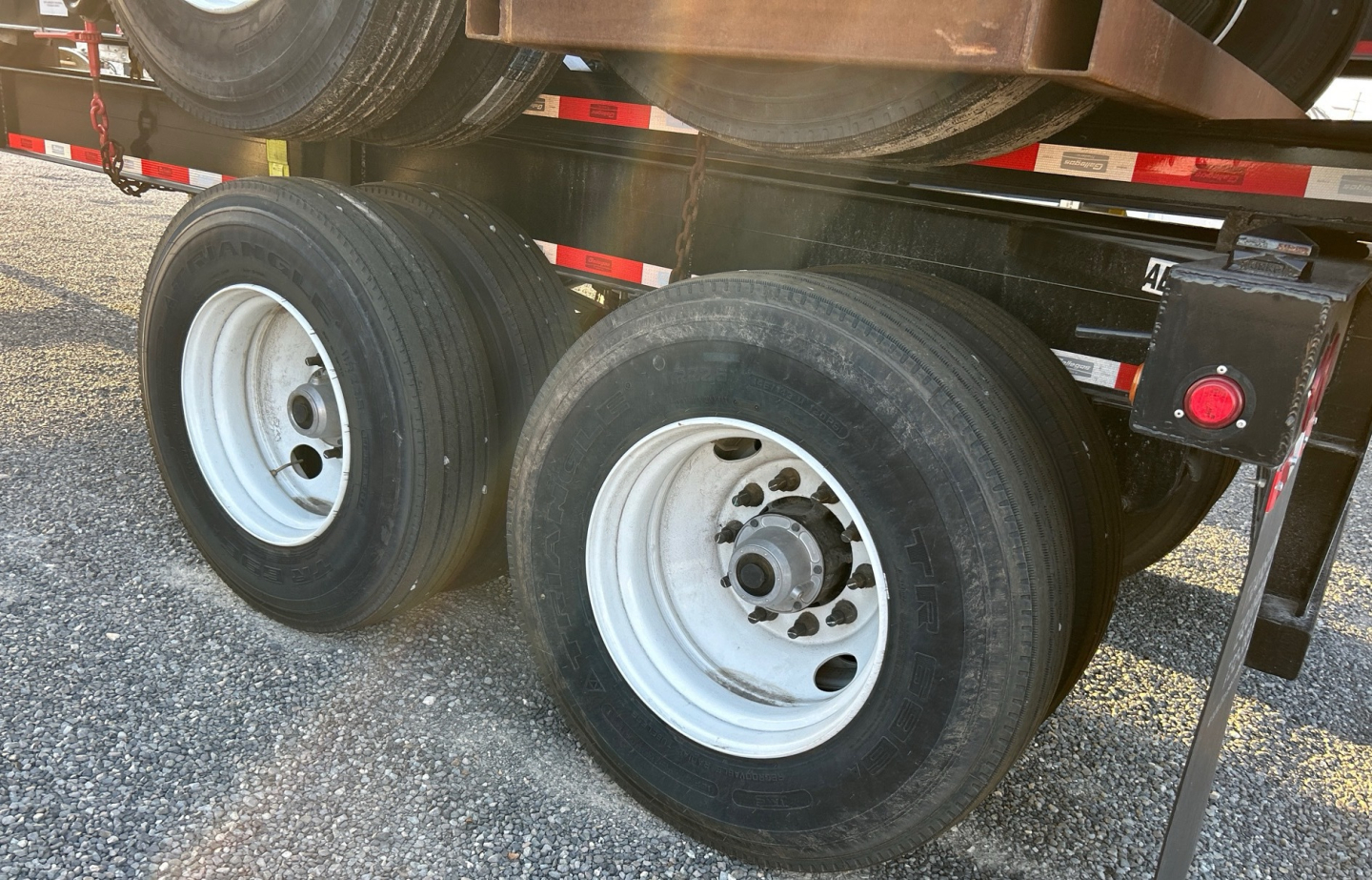 Dual rear axles of a trailer chassis with white steel wheels and black tires, showing undercarriage and support components.