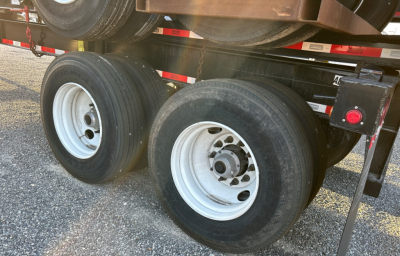 Dual rear axles of a trailer chassis with white steel wheels and black tires, showing undercarriage and support components.
