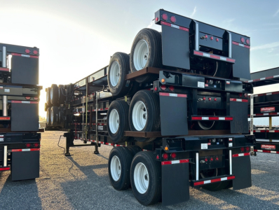 Intermodal container chassis trailer with multiple axles and spare wheels stack visible; rear and side view with dark blue frames and reflective tape.