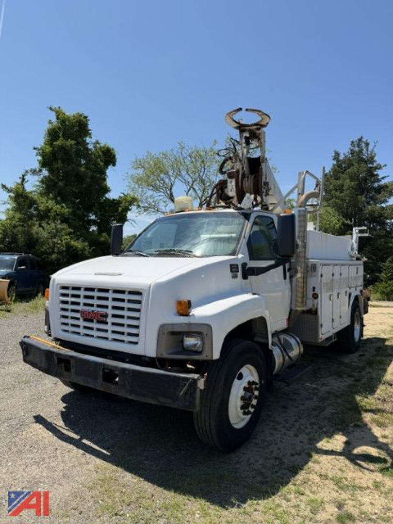 GMC C8500 digger truck in service condition with mounted drilling derrick on bed, white cab and utility body, front view showing grille and headlights.