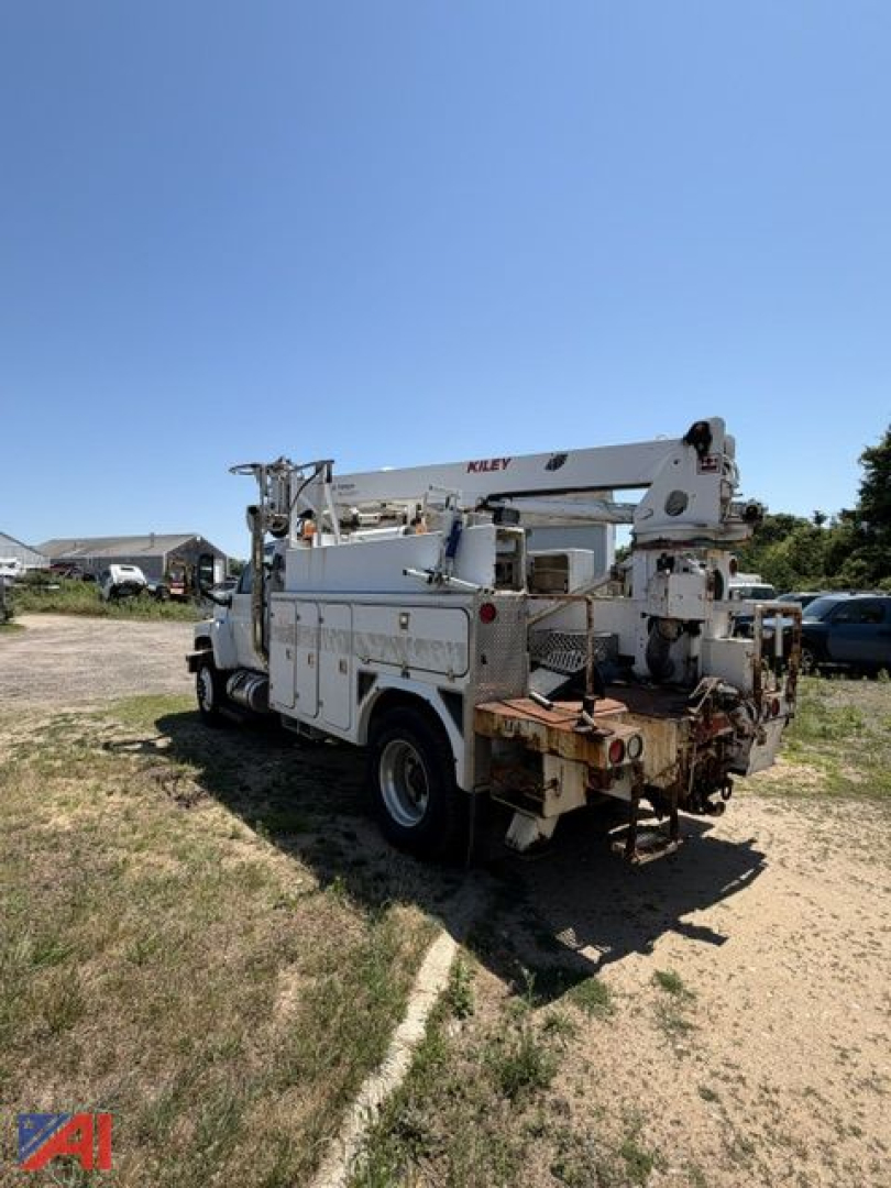 Rear/side view of a white GMC C8500 digger truck with crane boom extendedOverhead, utility compartments and toolbox visible.