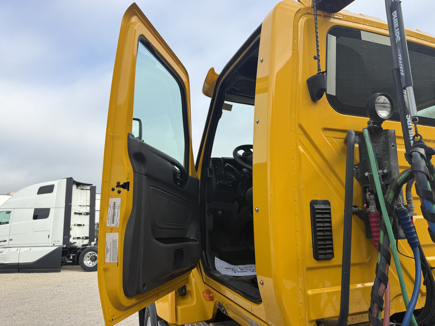 Interior of a yellow 2019 International LT cab with door open, showing steering wheel and dashboard area; outside truck with other rigs in background.