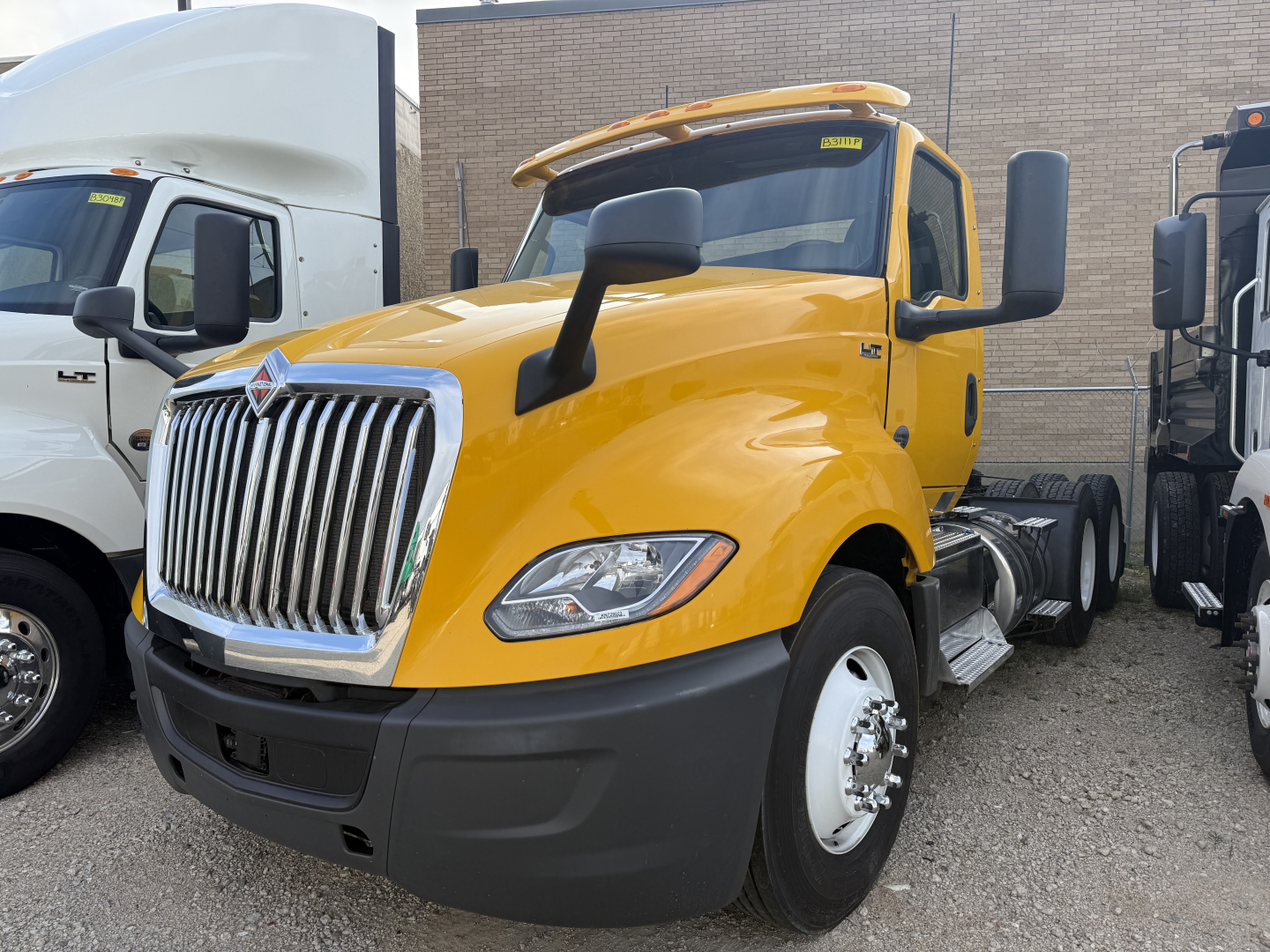 Yellow 2019 International LT conventional daycab tractor showing front grille and mirrors, with other trucks in background.