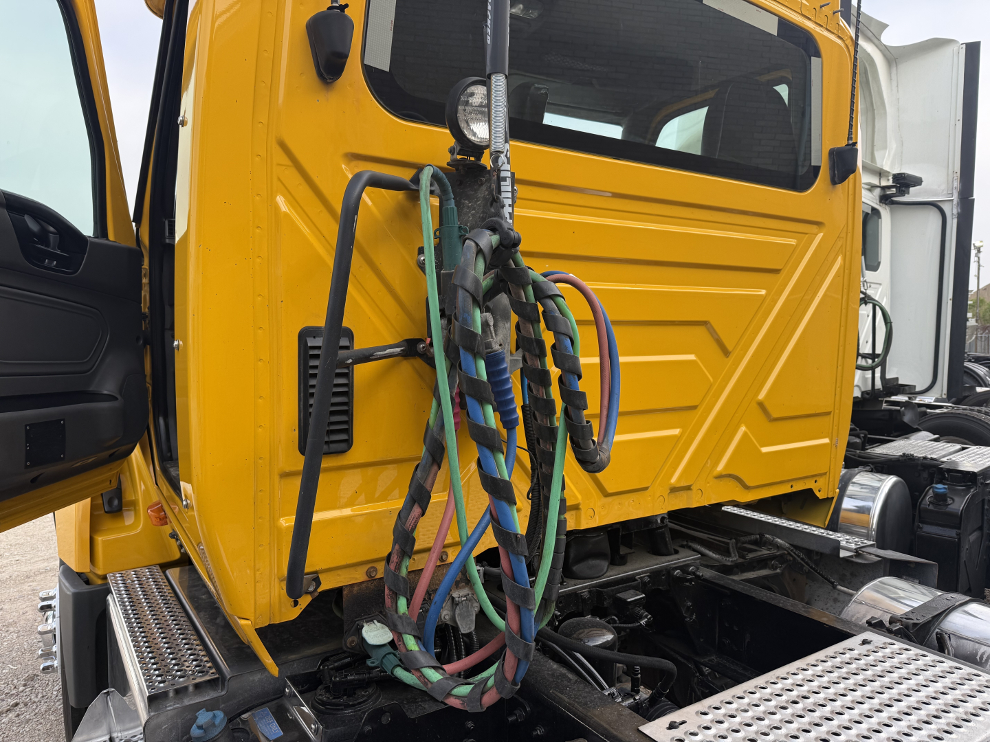 Truck cab interior and front of a 2019 International LT daycab showing yellow cab with attached colorful braided air lines and side steps.