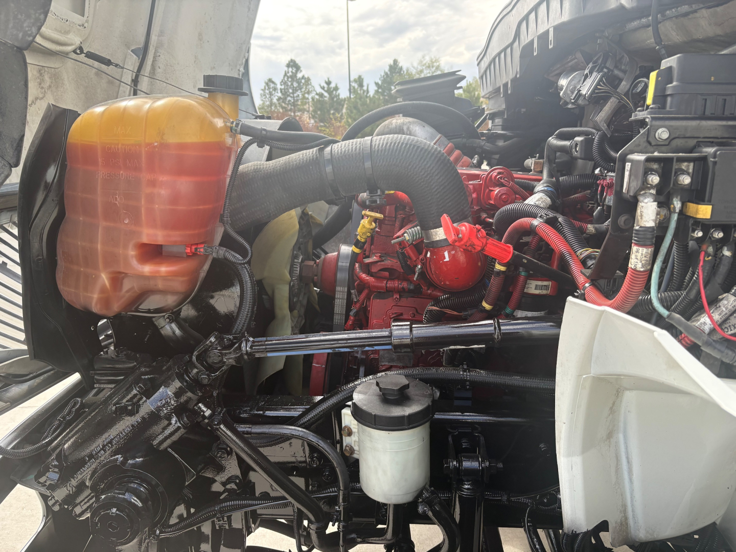 Truck engine bay showing coolant reservoir, red engine components, hoses, and white plastic air intake housing in a refrigerated 2021 International MV607.