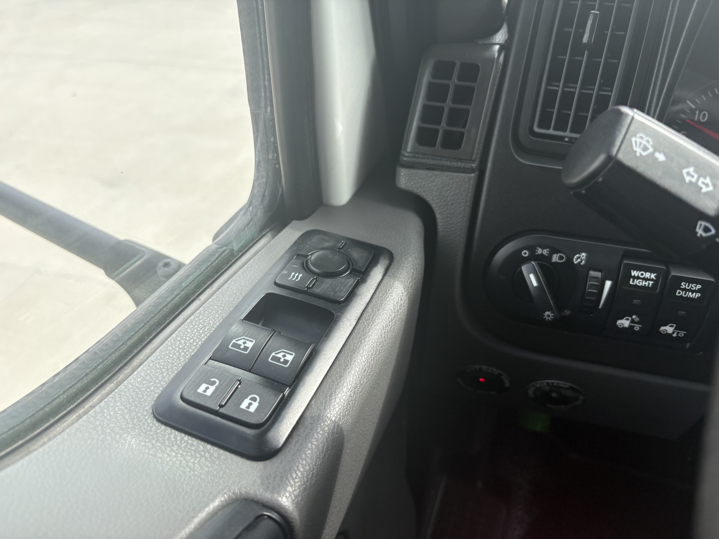 Truck interior door control panel and dashboard switches visible from driver’s seat. Includes window/lock controls on armrest and steering column with various dash icons.