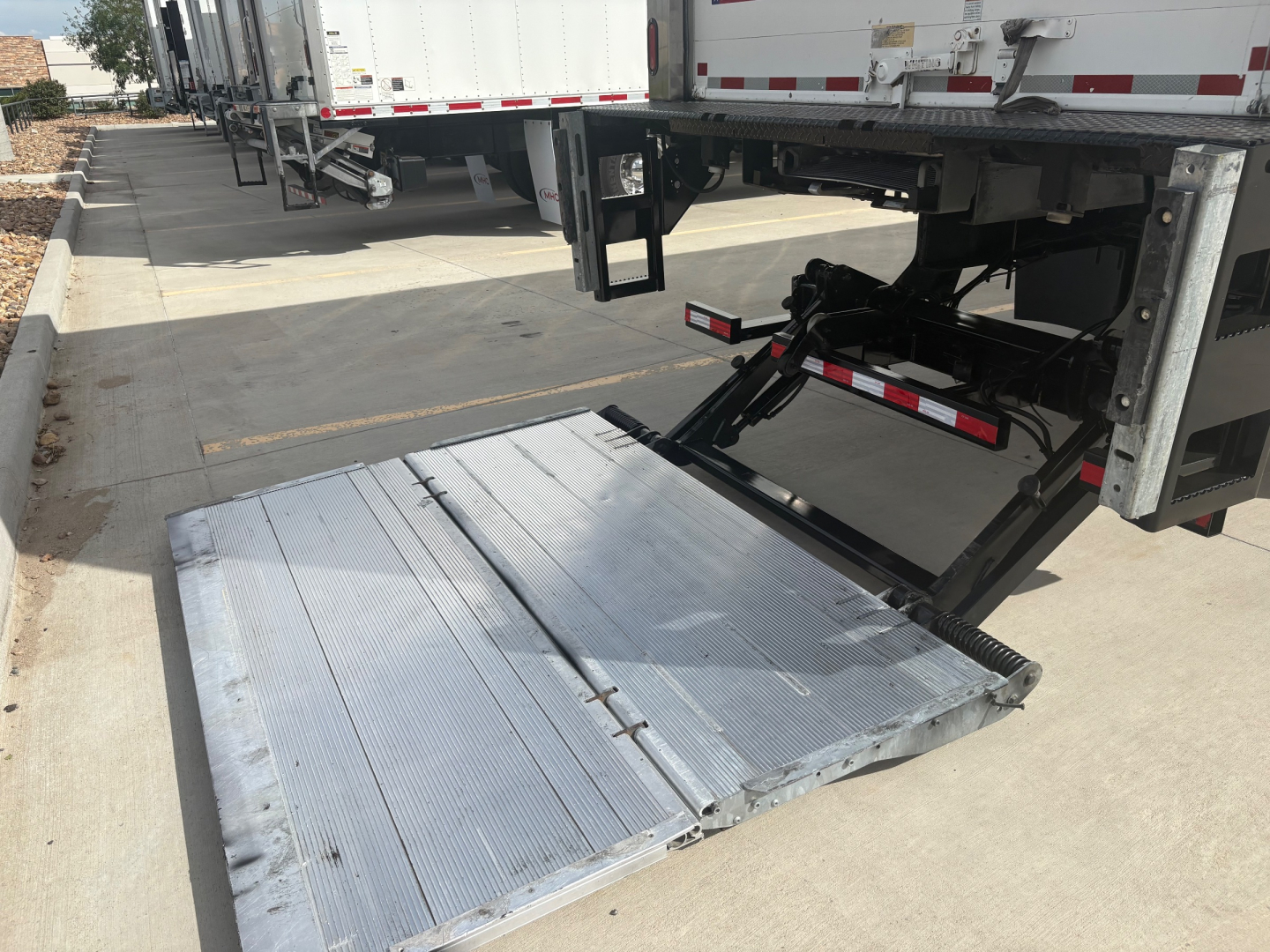 Truck liftgate deployed from a refrigerated International MV607 with a metal platform and hydraulic mechanism visible.