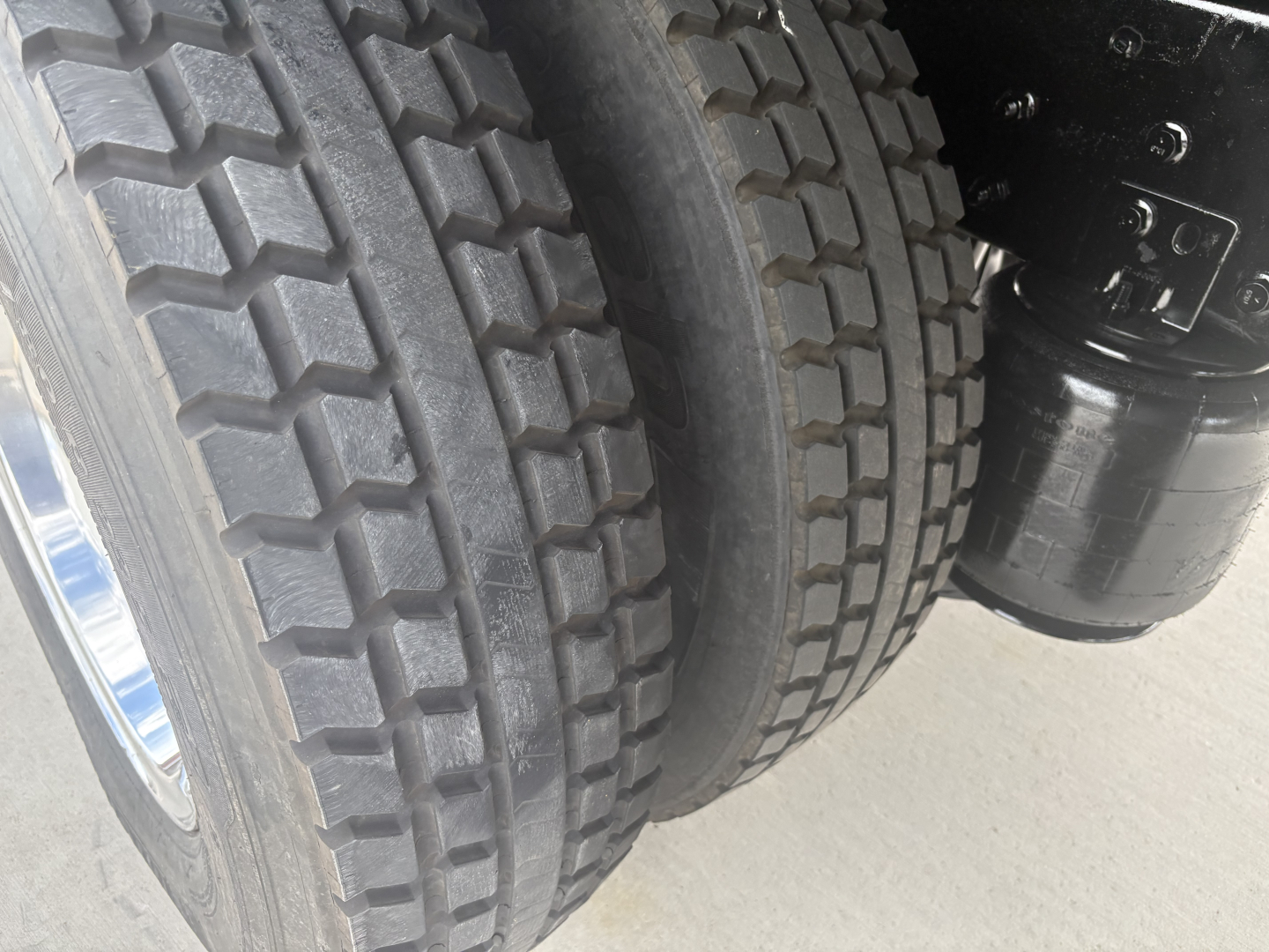 Truck rear dual tires and undercarriage components showing heavy tread tires and a black cylindrical component, part of the drivetrain or suspension on a refrigerated 2021 International MV607.